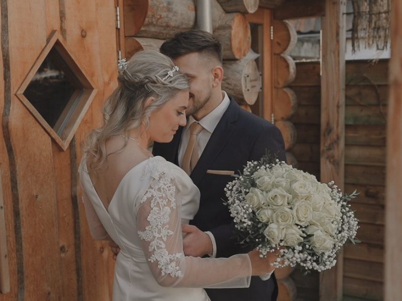 Bruid en bruidegom delen een teder moment voor een houten chalet, met een boeket van witte rozen in haar hand. door Lavender Photography. bruiloft fotograaf . trouwfotograaf . fotograaf bruiloft . fotograaf buiten bruiloft . huwelijksfotograaf . wedding fotograaf . loveshoot fotograaf Professionele bruiloftsfotograaf