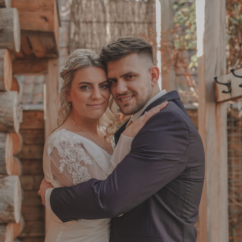 Bruid en bruidegom delen een teder moment voor een houten chalet, met een boeket van witte rozen in haar hand. door Lavender Photography. bruiloft fotograaf . trouwfotograaf . fotograaf bruiloft . fotograaf buiten bruiloft . huwelijksfotograaf . wedding fotograaf . loveshoot fotograaf Professionele bruiloftsfotograaf