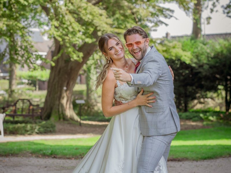 Bruid en bruidegom lachen en omhelzen elkaar vrolijk in een zonnig park op hun trouwdag. door Lavender Photography. bruiloft fotograaf. trouwfotograaf. fotograaf bruiloft. fotograaf buiten bruiloft. huwelijksfotograaf. wedding fotograaf. loveshoot fotograaf