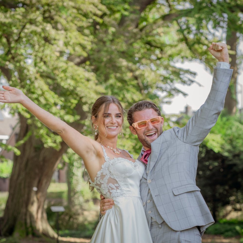 Bruid en bruidegom juichen van geluk in een zonnig park, vastgelegd tijdens hun bruiloft door Lavender Photography. bruiloft fotograaf